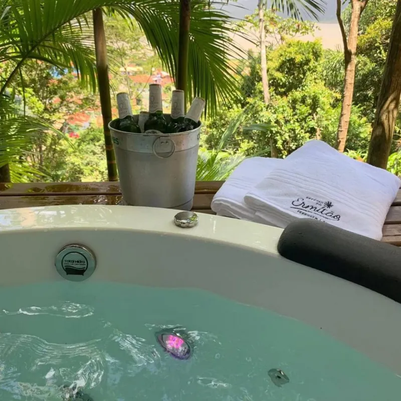 Ofurô aquecido com hidromassagem e toalhas com a marca do Refúgio, de frente para o bosque
