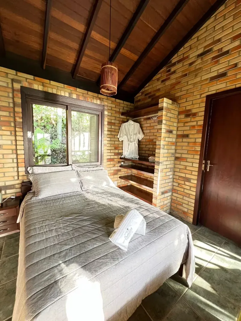 Suíte 01 com cama de casal, paredes de tijolo e teto de madeira